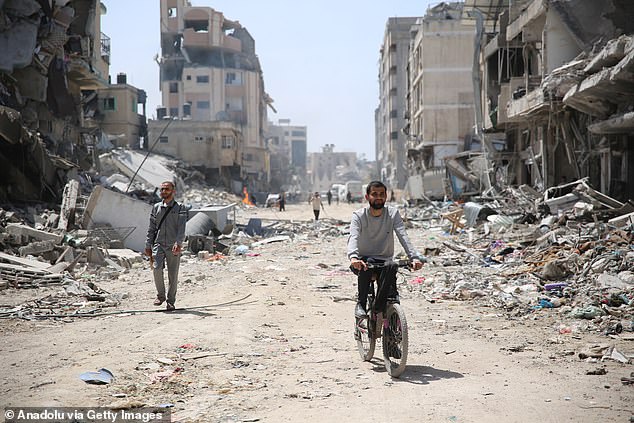 A man rides a bicycle near the rubble of the damaged building as the area around Al-Shifa Hospital is destroyed in Gaza City, Gaza.