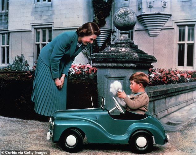 Queen Elizabeth watches her son, Prince Charles, driving a toy car in the grounds of Balmoral Castle.
