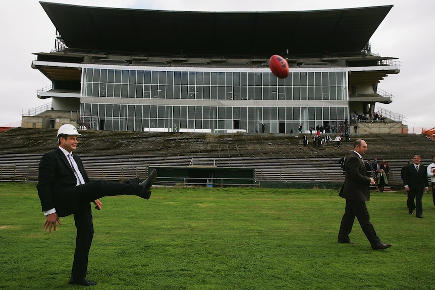 Helmeted Steve Bracks kicks a football at Waverley Park.
