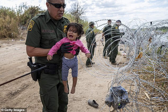 A U.S. Border Patrol agent holds a Venezuelan girl as her parents cross the barbed wire at the U.S.-Mexico border.