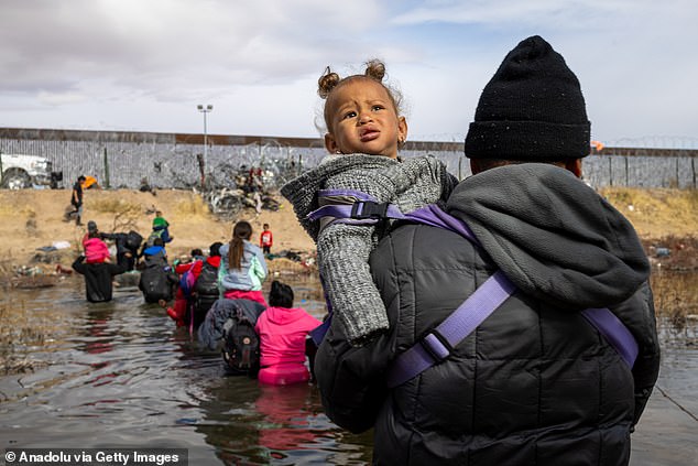 Migrant crosses the Rio Grande holding his daughter in the air to prevent her from getting wet