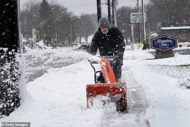 The intense storm surge that began Wednesday is expected to accumulate snow, rain, sleet and strong winds through Thursday. A man is seen using a snow blower to clear sidewalks in Green Bay, Wisconsin.