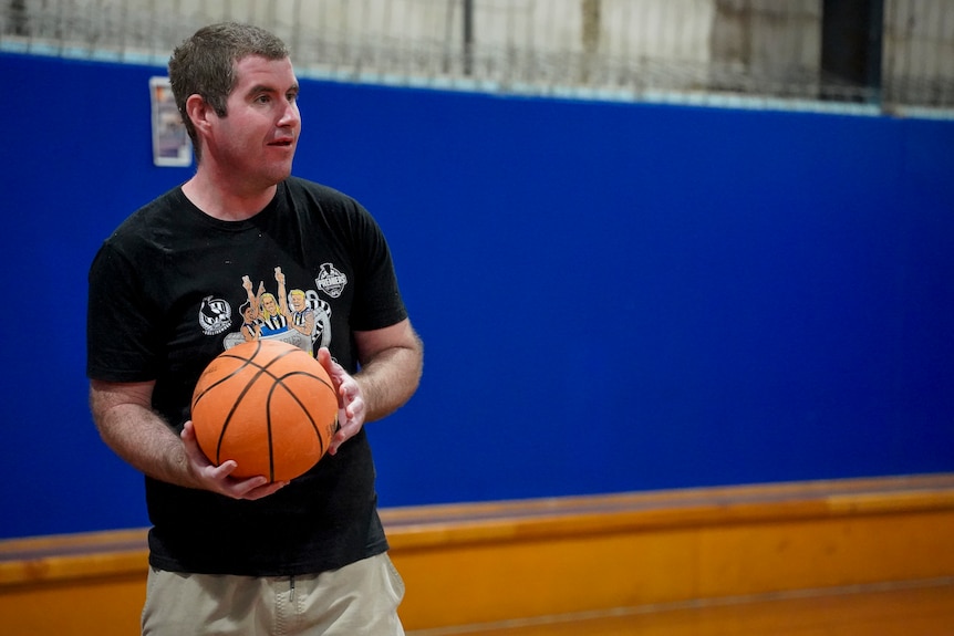 A man in a black t-shirt holds a basketball on the court.