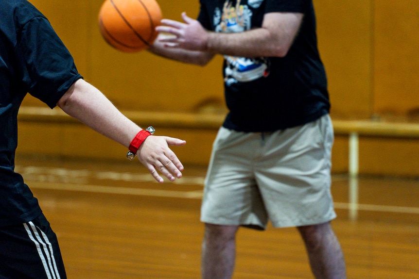 An outstretched hand with a wristband in the foreground and a person holding a basketball in the background.