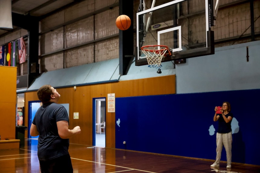 A young man shoots a basket and watches the ball head toward the net.