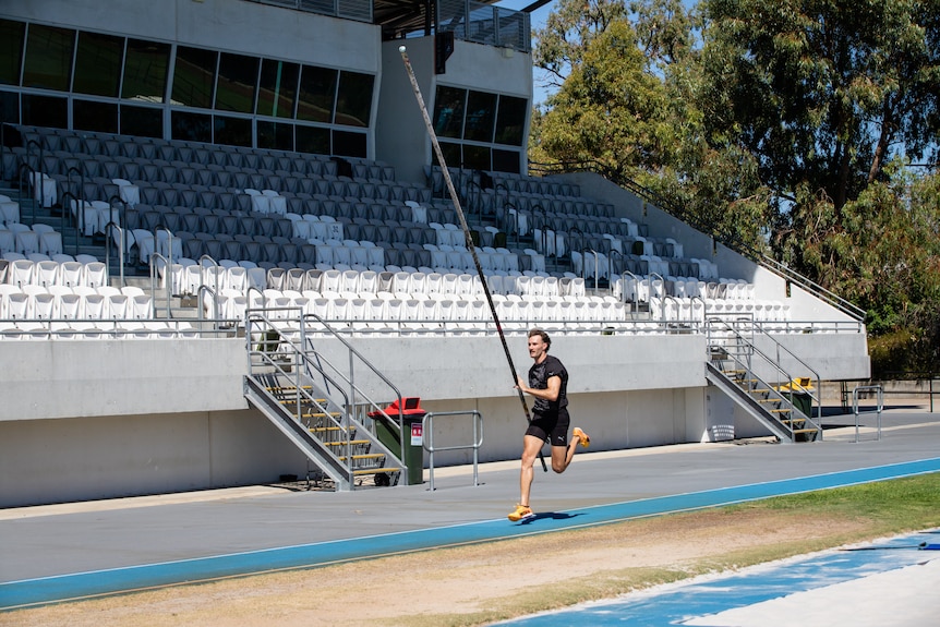 A man in sportswear trains in an athletics stadium on a sunny day.