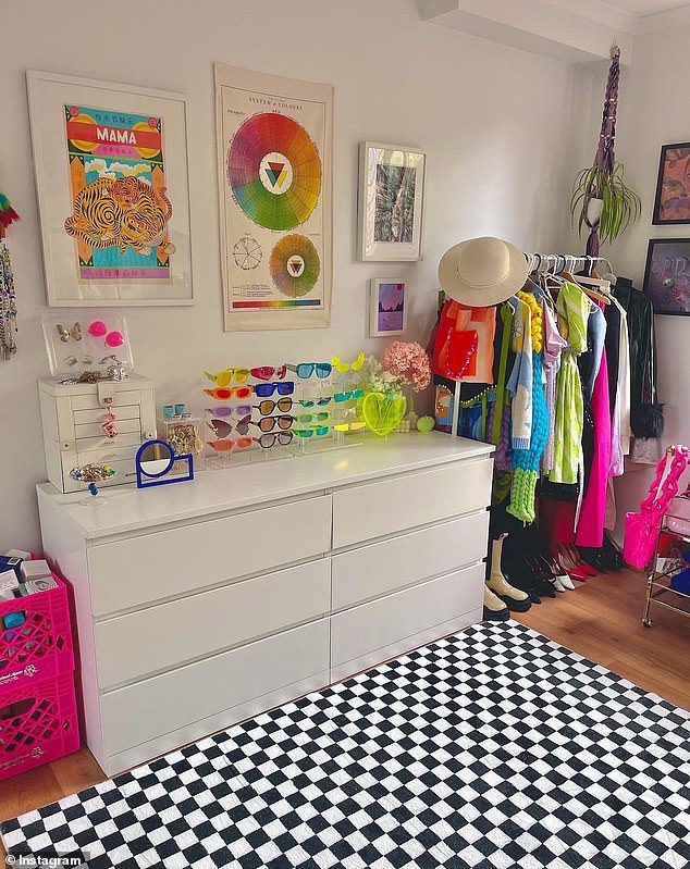 In her beauty salon there is an explosion of color in every corner with a clothes rack, a cup holder, a checkered rug, hot pink boxes and prints on the walls.