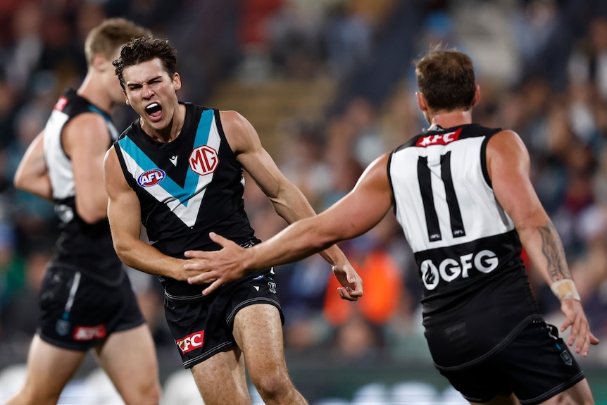 Port Adelaide captain Connor Rozee roars in triumph as his teammate extends his hand in recognition after a goal.