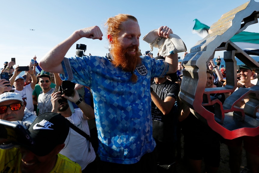 A red-haired man cheering surrounded by a crowd. 