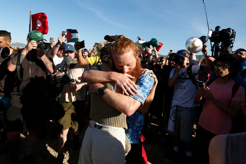 A red-haired man hugging a person, surrounded by a crowd of photographers. 