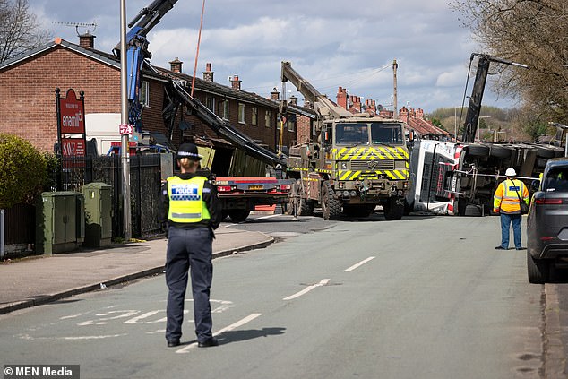 A police officer watches as emergency services attempt to remove the crane embedded in the property.