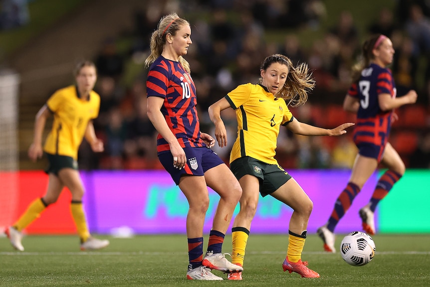 A Matildas defender rushes to pressure an American player who quickly pushes the ball away.