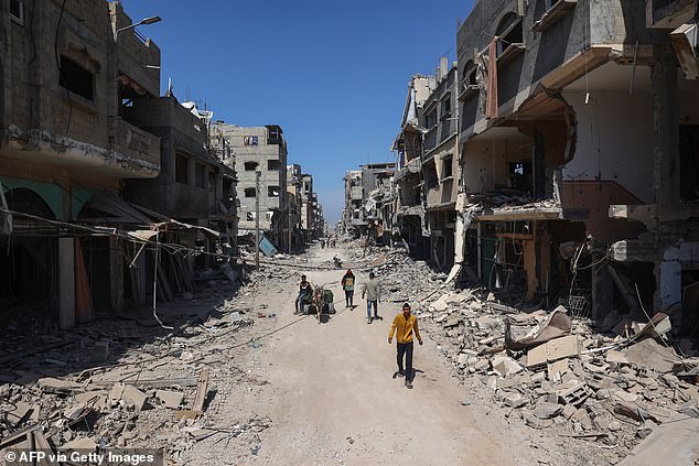 Palestinians use a road lined with damaged and destroyed buildings in Khan Yunis on April 7, 2024.