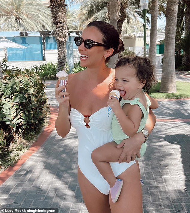 Combing her long brunette tresses into a sleek bun, Lucy wore a stylish pair of stylish black pants as she held her smiling little one for a photo.