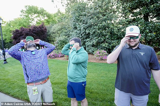Friends try on eclipse glasses during a practice round for the Masters Tournament