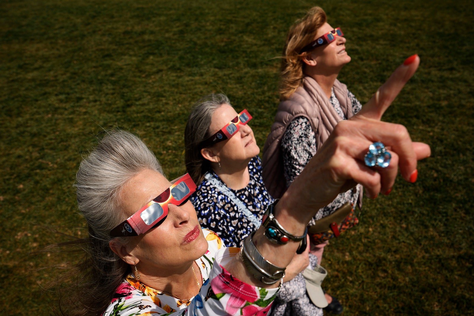 Photo of three women watching the solar eclipse near the base of the Washington Monument on the National Mall