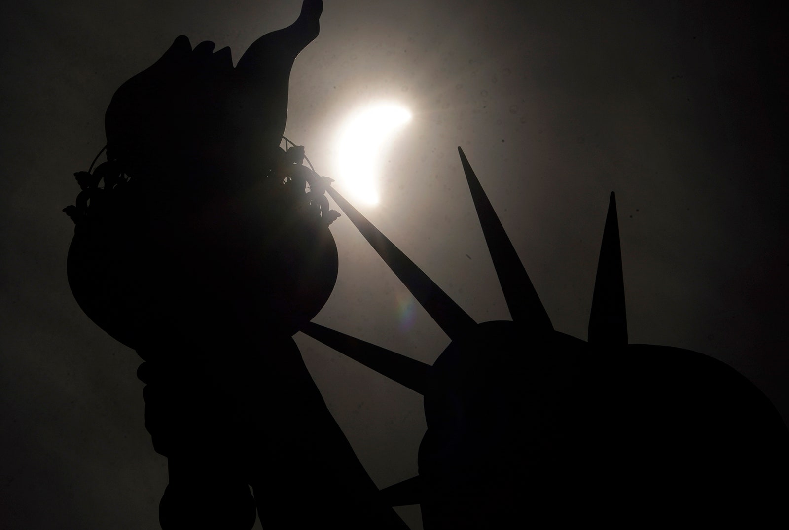 Photo of a partial solar eclipse moving across the sky near the Crown of the Statue of Liberty on Liberty Island