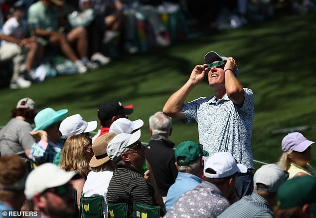 Videos shared on social media showed people looking up at the grayish sky to catch a glimpse of the phenomenon that left only the sun's outer atmosphere visible, briefly obscuring the outside during the day.  In the photo, people wear protective glasses to observe the eclipse at the Masters in Augusta, Georgia.