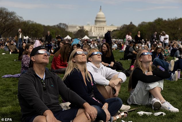 People on the National Mall watch a partial solar eclipse, with the United States Capitol Building seen behind, in Washington, DC, United States. The narrow path of totality passed through 13 US states.