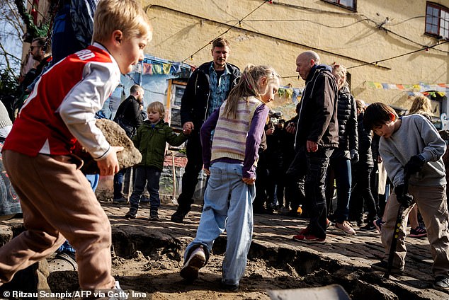 Children participate as residents of the Christiania neighborhood unearth the cobblestones of Pusher Street.