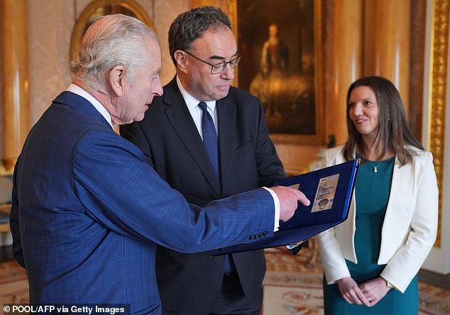 King Charles III reacts to the first banknotes with his portrait as Bank of England Governor Andrew Bailey shows him the leather-bound booklet.