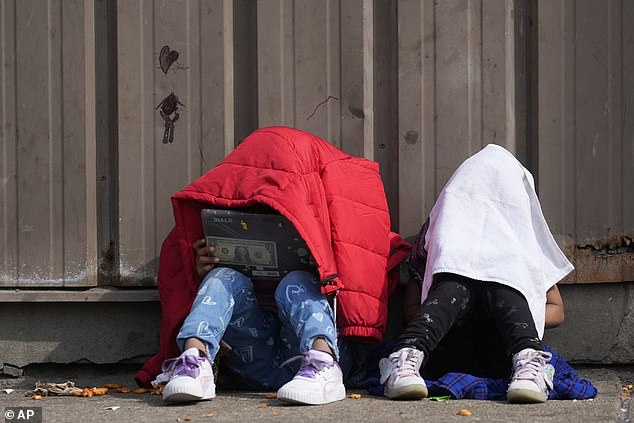 Children cover their heads as they sit outside a migrant shelter on Wednesday, March 13, in Chicago's Pilsen neighborhood.