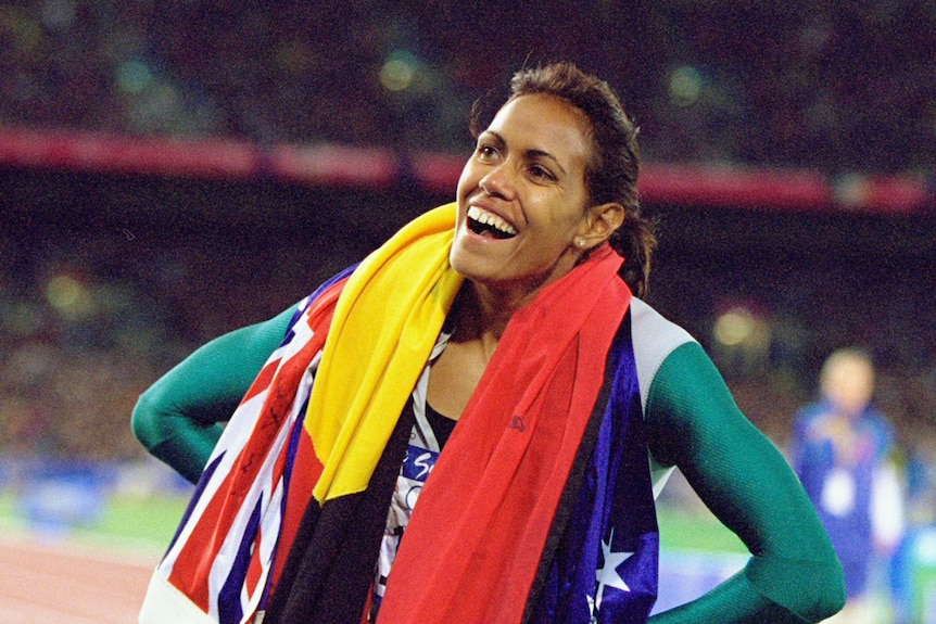 Cathy Freeman smiling with the Aboriginal and Australian flag around her neck.