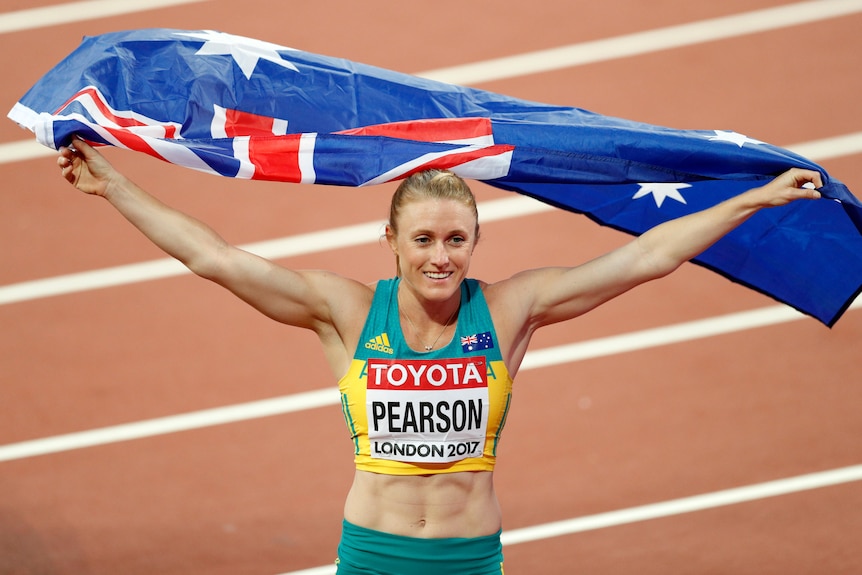 Sally Pearson on a running track holding the Australian flag above her head.