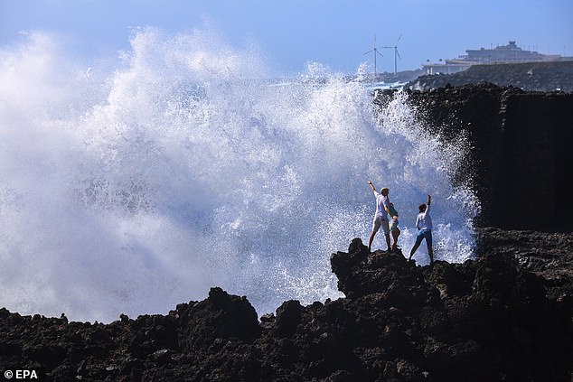 Tourists pose for photographs as high waves crash on the coast of La Palma, Gran Canaria, Spain, on Wednesday.