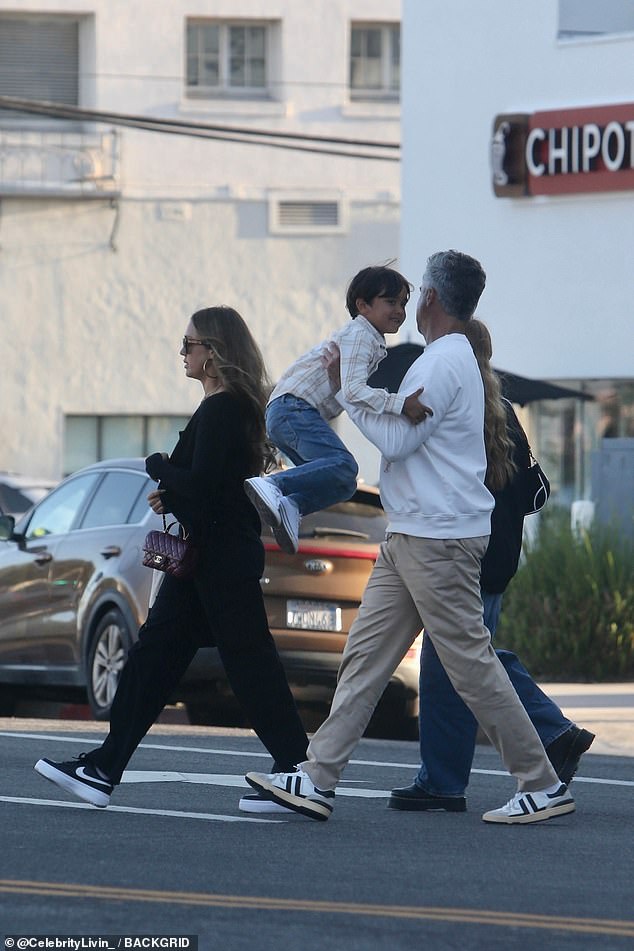 Meanwhile, her husband was dressed in a white sweater, khaki pants, and sneakers, and was photographed sweetly holding their son in his arms as they crossed the street.