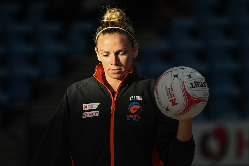 Jo Harten looks down and holds the ball in her left hand as the sun floods half of her face in a dark stadium.
