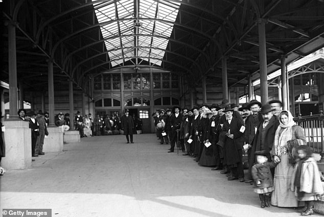 Pictured: A large group of immigrants lined up outside waiting to be taken off Ellis Island, by Edwin Levick, Ellis Island, New York, 1907.