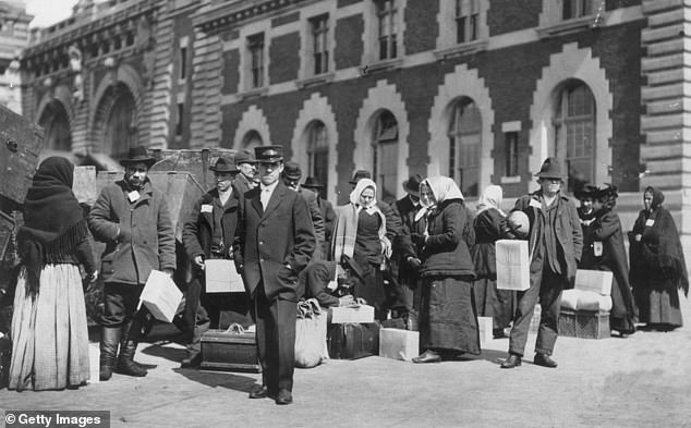 Pictured: Immigrants with trunks outdoors in front of a building on Ellis Island in 1907.