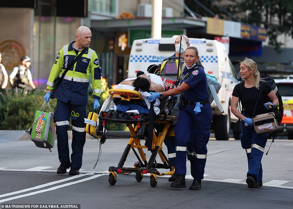 In the image, paramedics carry a victim to an ambulance.