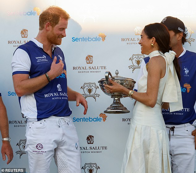 The Duchess of Sussex, 42, smiled with joy as she presented the trophy to her husband.