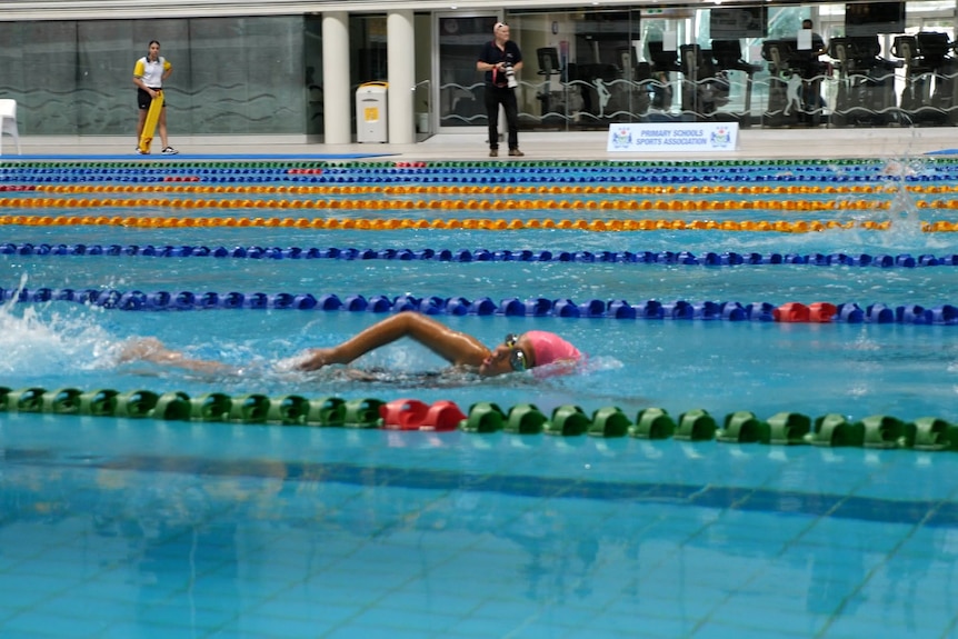 A young woman breathes while swimming freestyle in an Olympic pool.