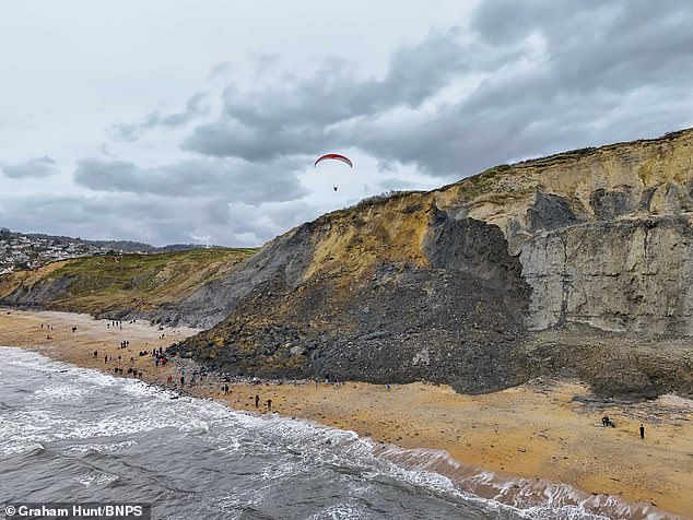 A paraglider flies over the top of the landslide near Charmouth Beach in Dorset yesterday.