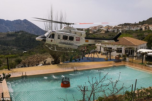 A helicopter fills with water from a pool as crews work to fight the fire.