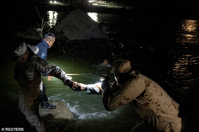 A member of the Mexican National Guard turns on a light as a police officer uses a stick to rescue a Columbia woman who was being swept rapidly downstream by the strong current while trying to cross the Rio Grande.