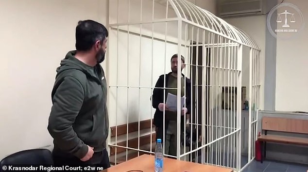 Lyutyi is seen in a cage in a courtroom in the middle of his trial.