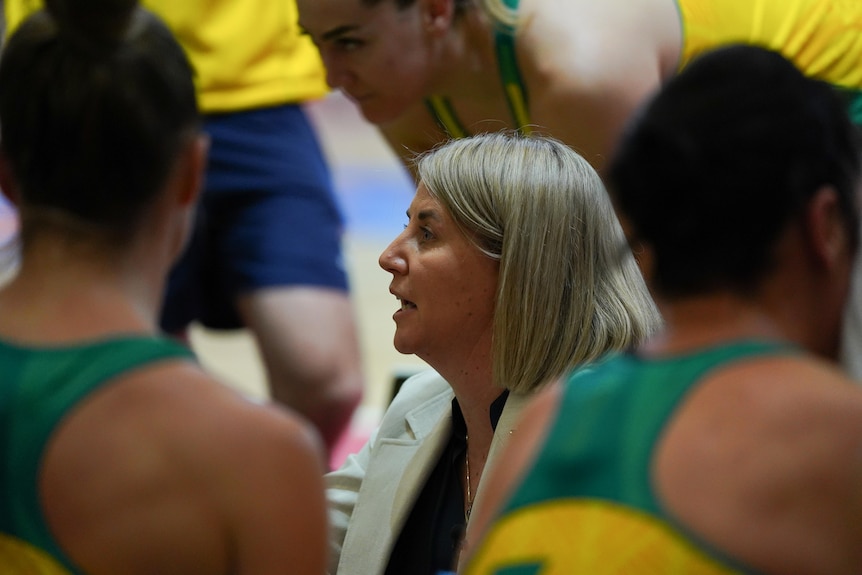 The image focuses on an Australian netball coach speaking surrounded by her players during a match.