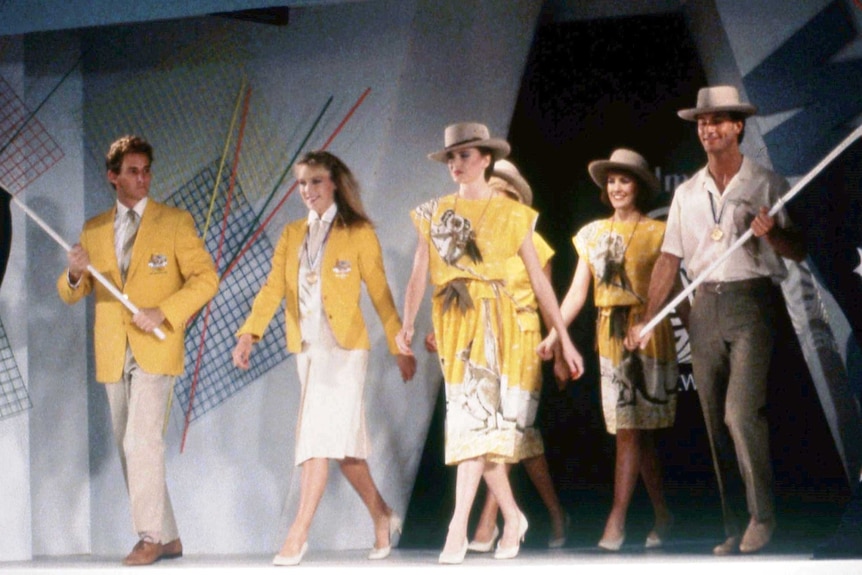 Four people walking towards the opening ceremony stage wearing yellow animal dresses and holding Australian flags.