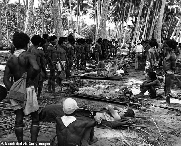 Local people watch the wounded Americans. and Australian soldiers placed on a row of stretchers. Papua New Guinea, December 1942