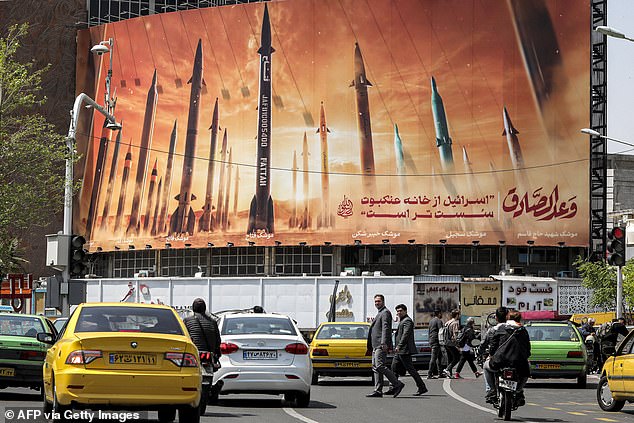 Motorists drive their vehicles past a sign showing in-service Iranian ballistic missiles with names, with text in Arabic. "the honest [person's] promise" and in Persian "Israel is weaker than a spider web"at Valiasr Square in central Tehran on April 15, 2024