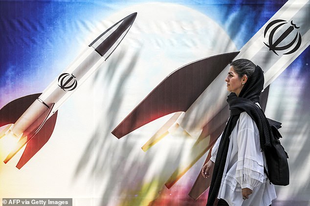 A woman walks past a banner depicting the launch of missiles with the emblem of the Islamic Republic of Iran in central Tehran on April 15, 2024.