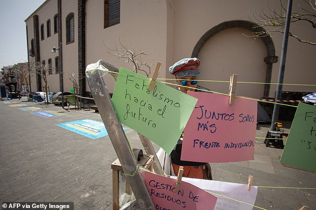 A man hangs signs written by protesters next to tents of activists on hunger strike to protest against mass tourism infrastructure in La Laguna, on April 13, 2024.