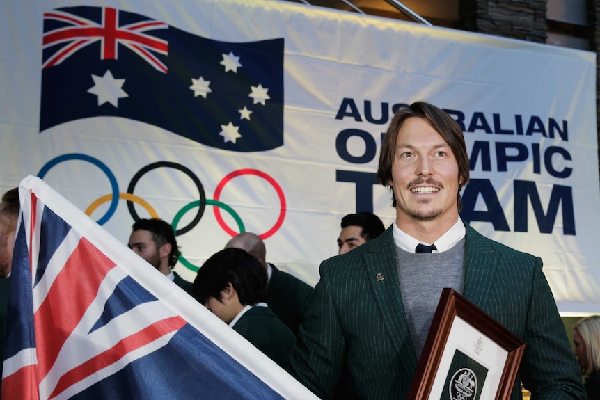 A man holds an Australian flag in front of the Olympic rings.