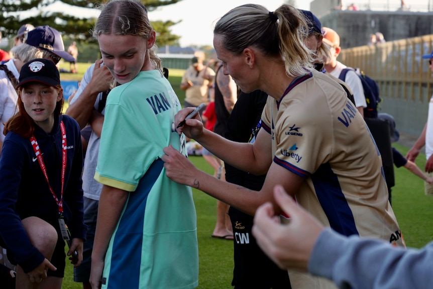 A soccer player signs a fan's shirt.