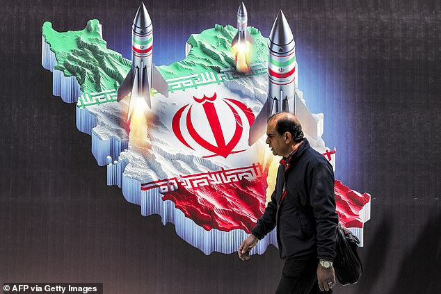 Iranian state media reported that the drone strikes took place on Friday. (Pictured: A man walks past a banner depicting missiles launched from a representation of the map of Iran)