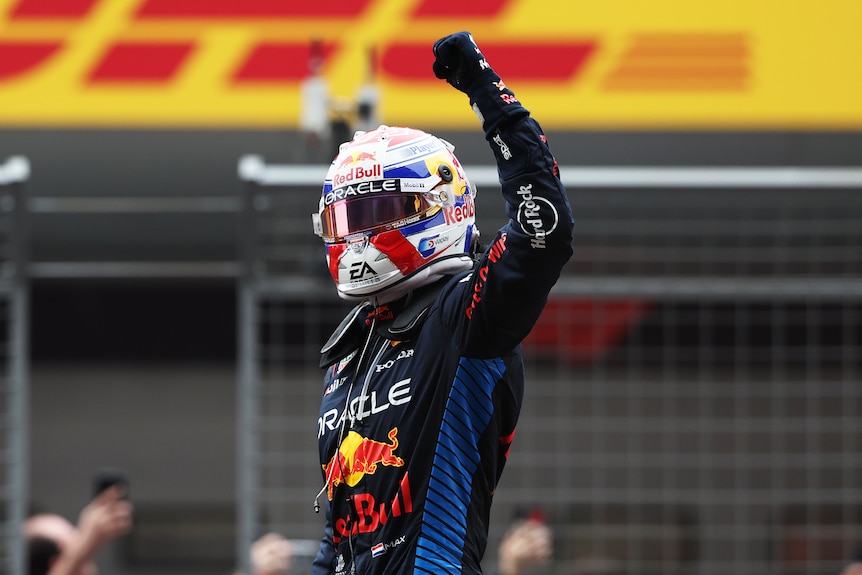 F1 driver Max Verstappen raises his fist in the air while standing in his car in China.